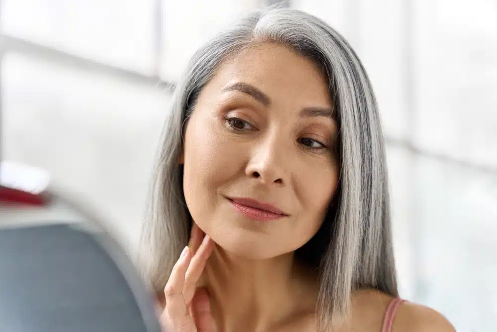 Mature woman touching her jawline, representing skin tightening with Ultherapy and radiofrequency treatments.