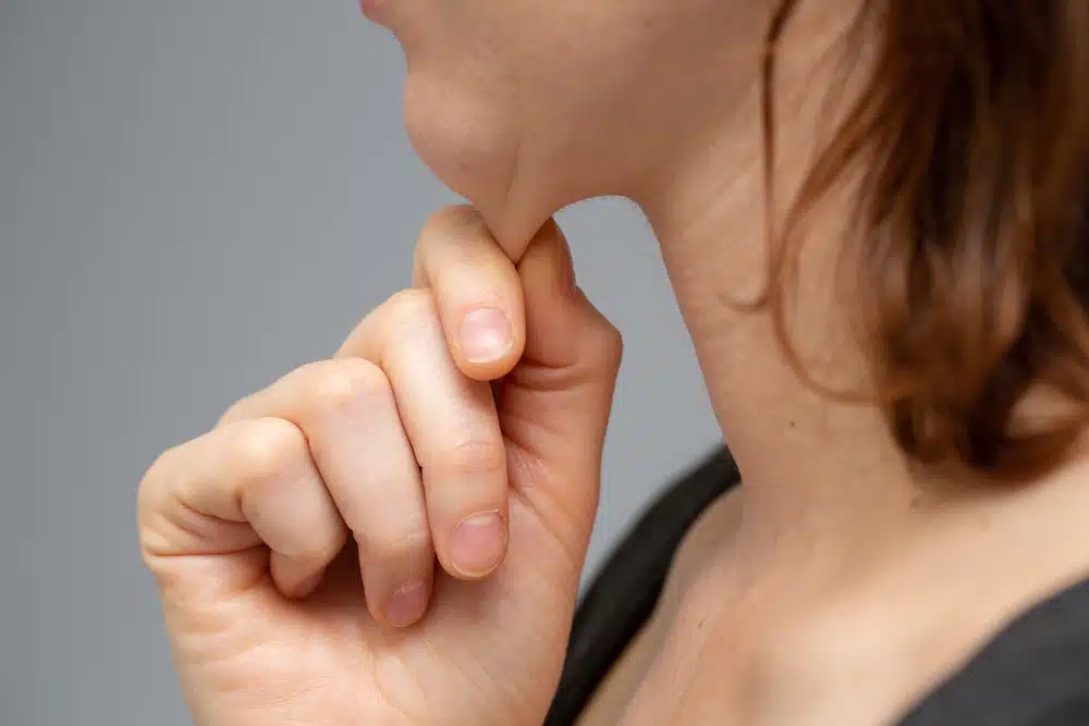 Close-up of a person pinching the skin under the chin, representing chin ptosis or witch's chin.