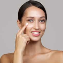 Woman gently pointing to her under-eye, clear skin, post-surgery care focus.