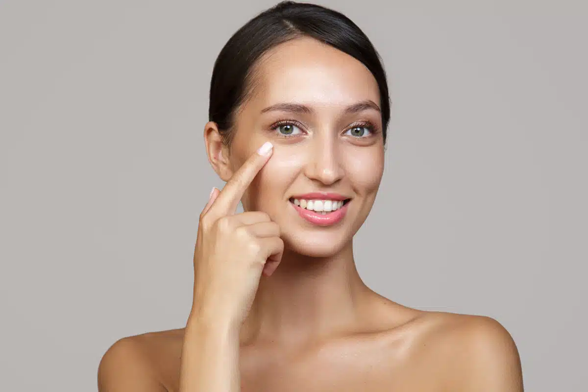 Woman gently pointing to her under-eye, clear skin, post-surgery care focus.