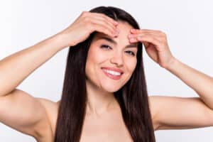 Smiling woman gently touches her brow area after minimal surgery.