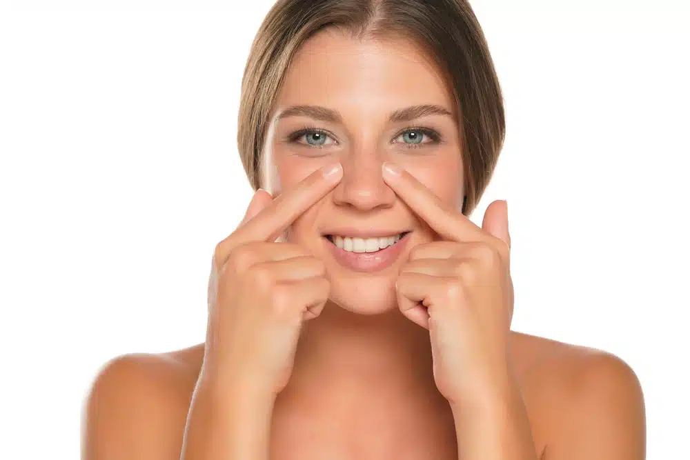 Woman smiling and pointing to her uneven nostrils, illustrating nostril asymmetry's effect on facial symmetry.