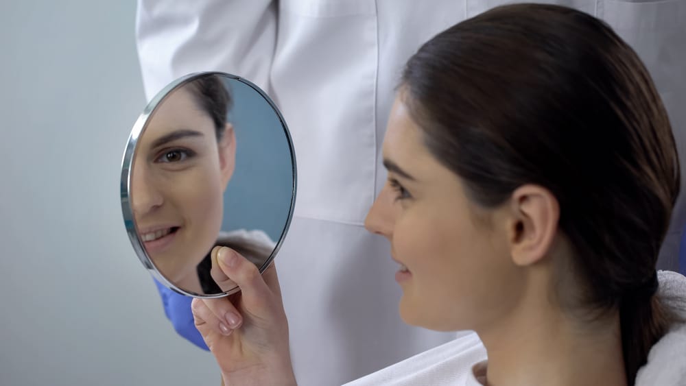 Patient views her finalized rhinoplasty results in mirror one year after surgery.