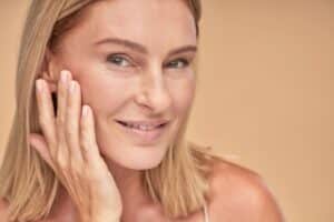 Smiling mature woman gently touching her face, representing pre-facelift preparation.