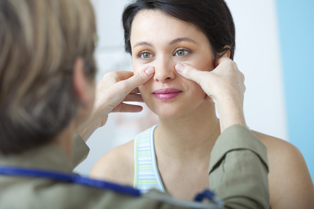 Doctor gently examines patient's nose six months into rhinoplasty recovery, checking for issues.