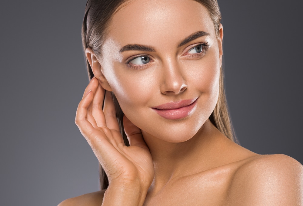  Woman gently touching her face, showcasing healthy skin post-nostril shaping surgery.