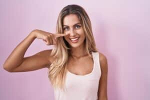 Smiling woman pointing to nose, representing potential rhinoplasty before and after.