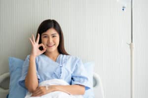 Smiling patient in a hospital bed giving an OK sign, emphasizing the importance of selecting the perfect month for surgery.