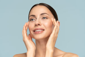 Woman touching her face with smooth skin, representing early signs of facial aging and facelift timing.