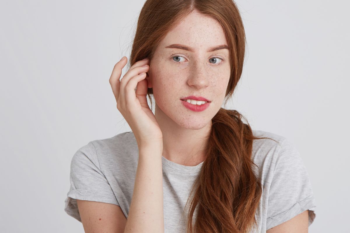 Young woman gently touching ear, demonstrating careful post-otoplasty behavior to protect healing surgical site.