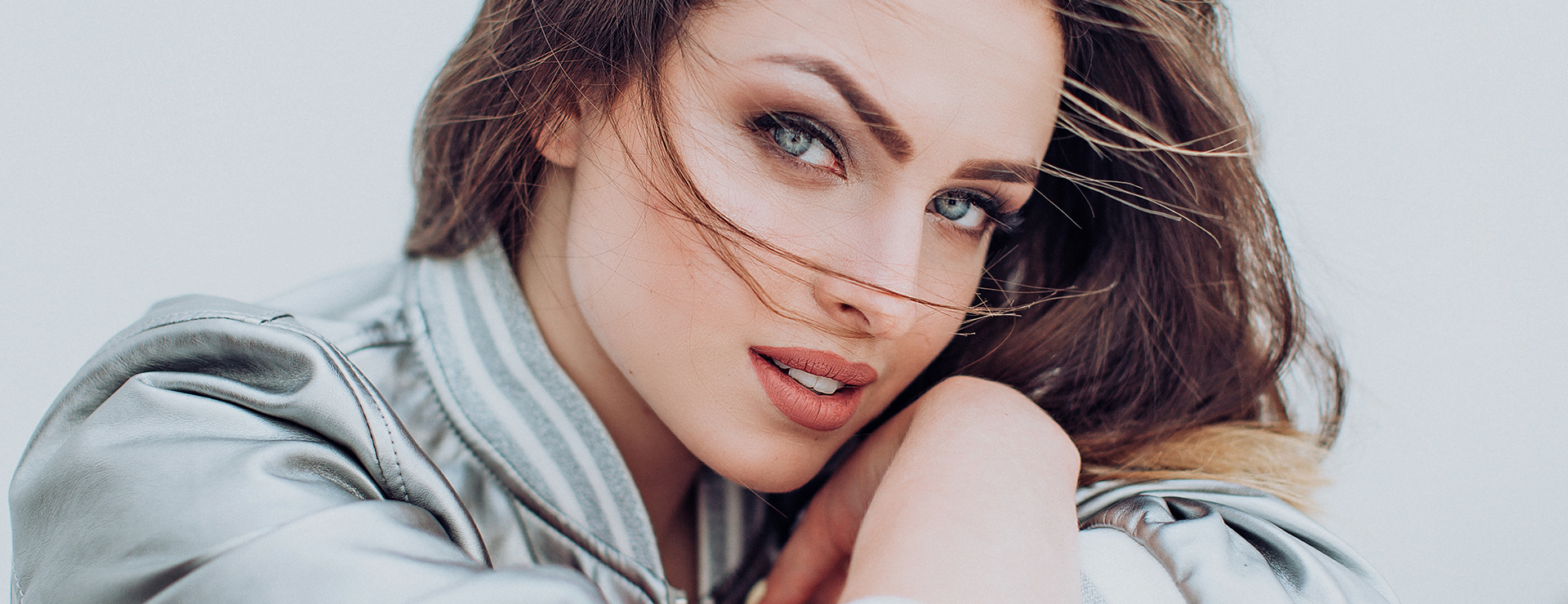 Close-up of a woman with striking blue eyes, soft makeup, and flowing hair exuding natural beauty.