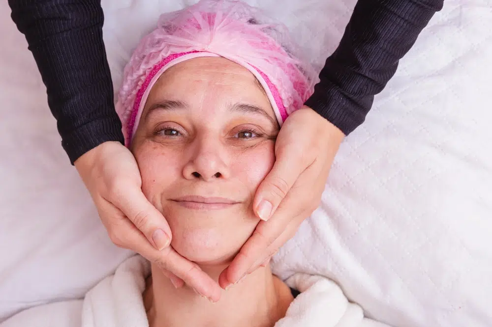 Middle-aged woman receiving facial evaluation, highlighting factors like skin laxity and tissue descent for facelift timing