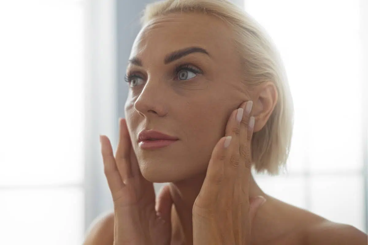 A woman with her eyes closed lightly touching her face to monitor the slow return of sensation and nerve regeneration following a facelift.
