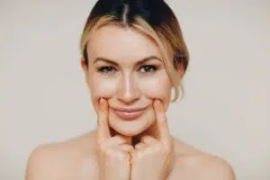 Woman gently pressing smile lines on cheeks, illustrating nasolabial folds and facial aging improvement concept